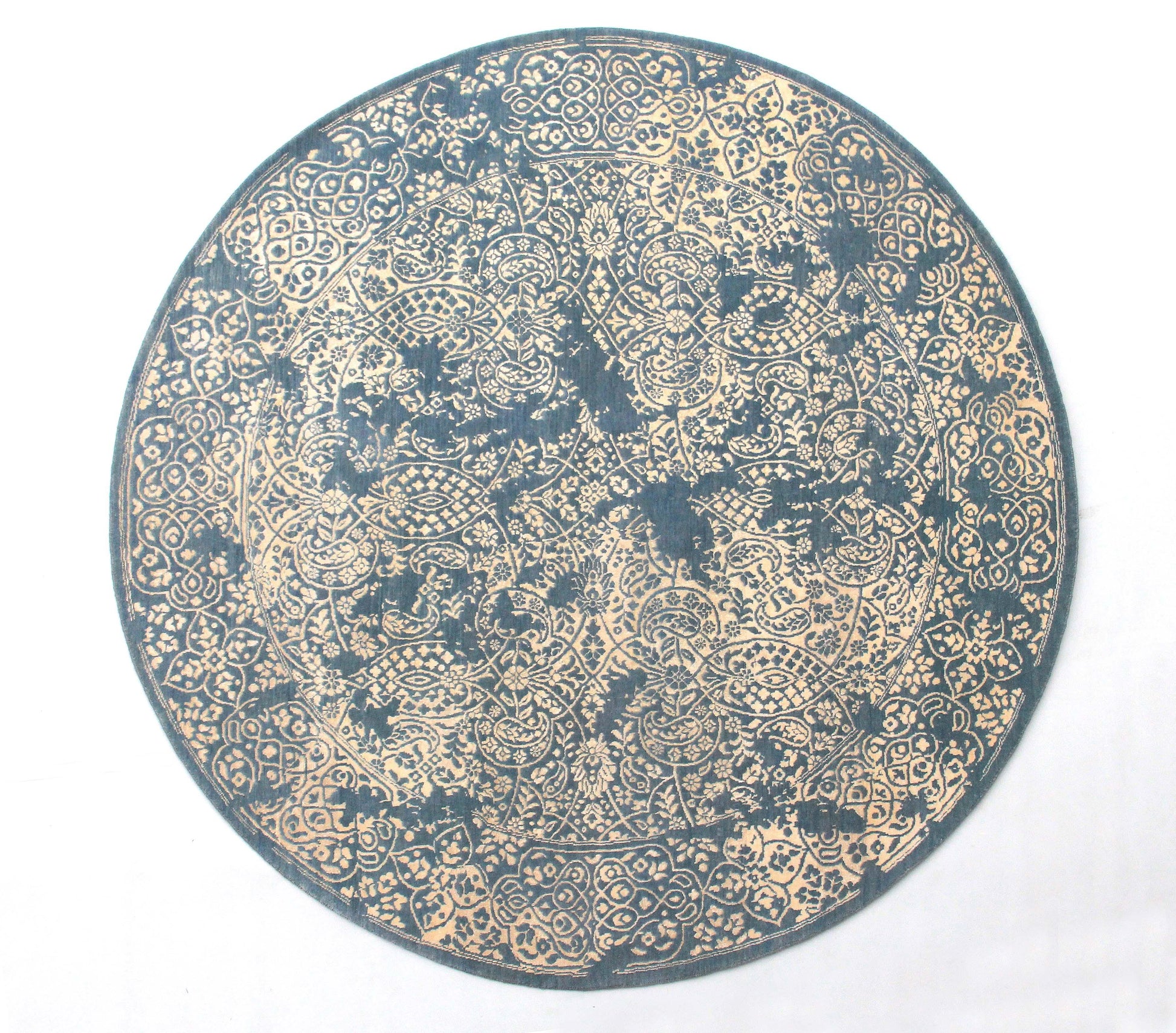A round, hand-knotted wool and silk rug with a paisley design in blue and beige colors.