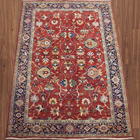 A traditional Persian-style area rug with a red field, navy blue borders, and intricate floral motifs in beige, green, and blue, laid flat on a brown wooden floor.
