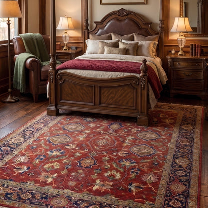 A large traditional oriental-style area rug with a red, navy, and beige floral pattern, styled in a warm, wood-paneled bedroom next to a four-poster bed.