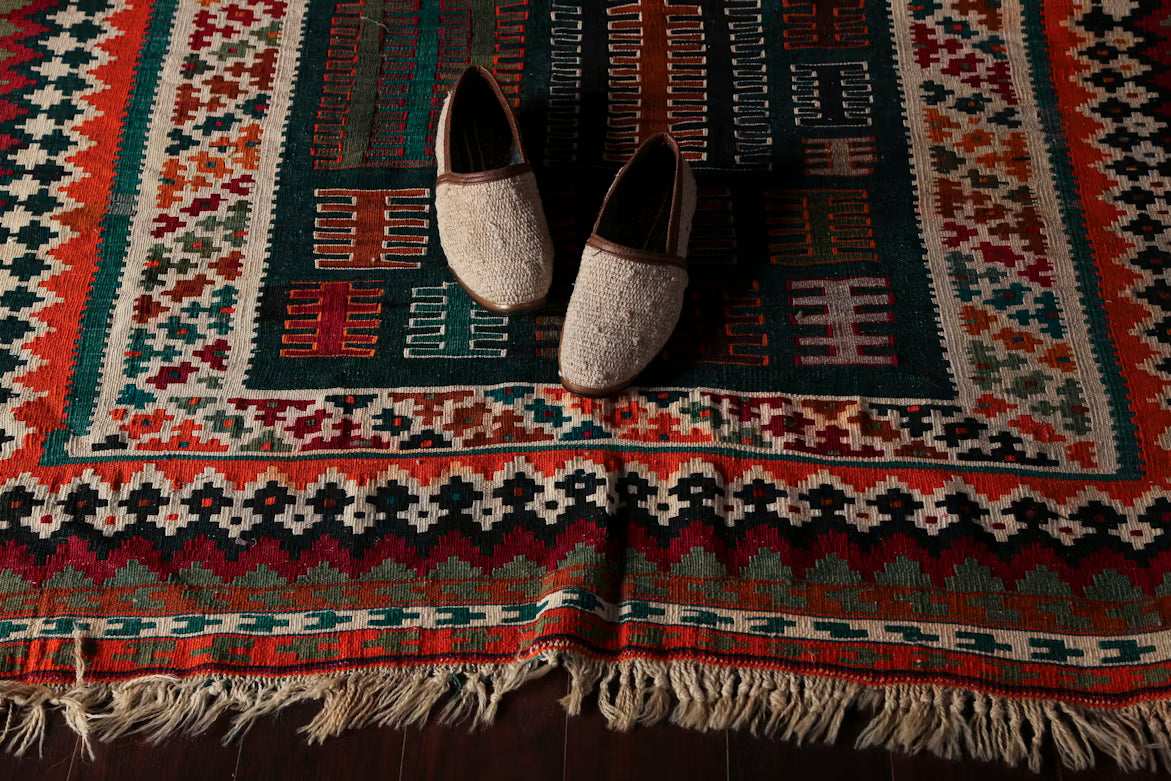 Traditional patterned area rug with intricate geometric motifs and fringe detailing, showcased prominently with a pair of woven slippers placed at the center | Cassimrug